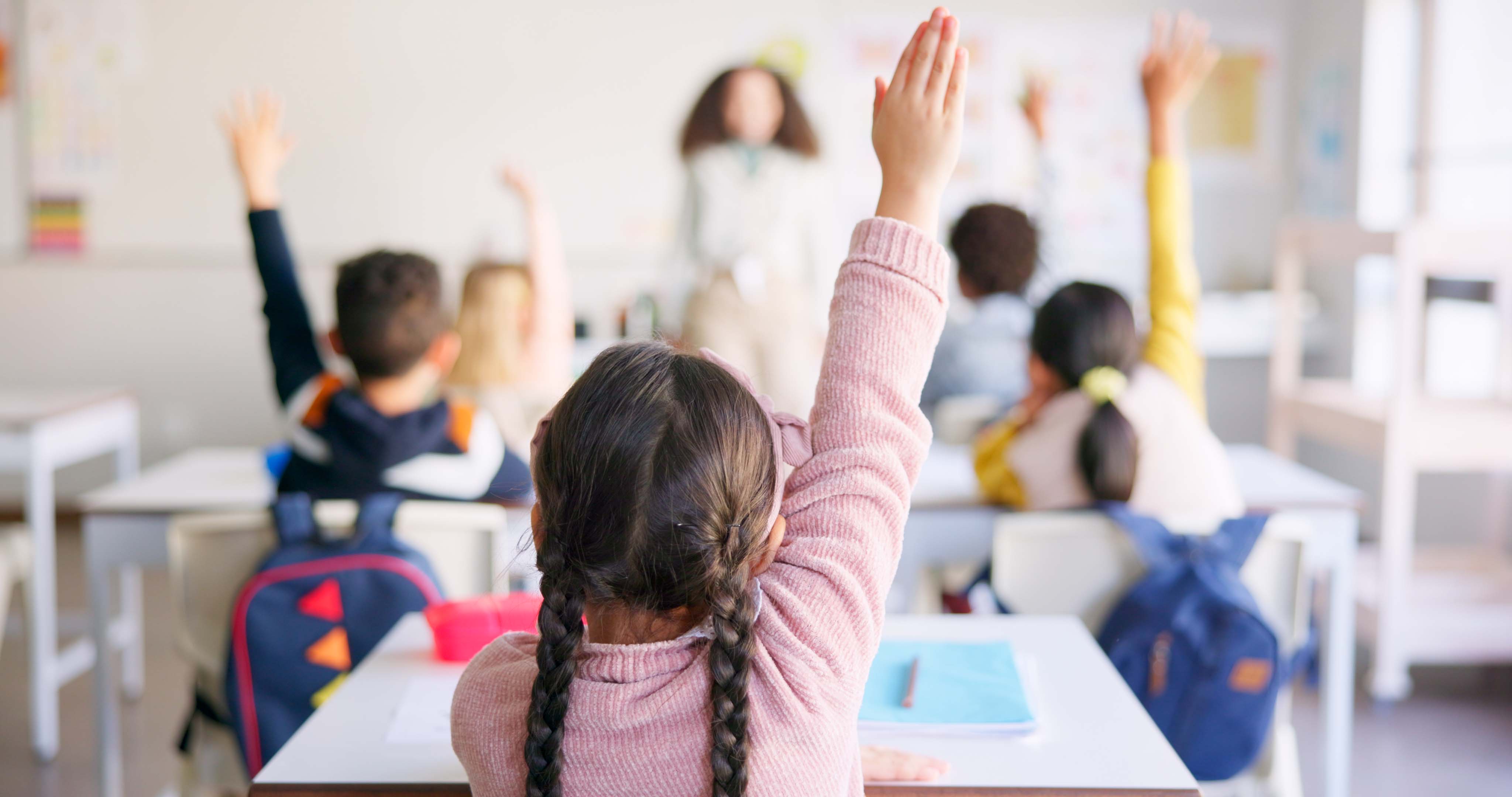 A child raises her hand in a classroom